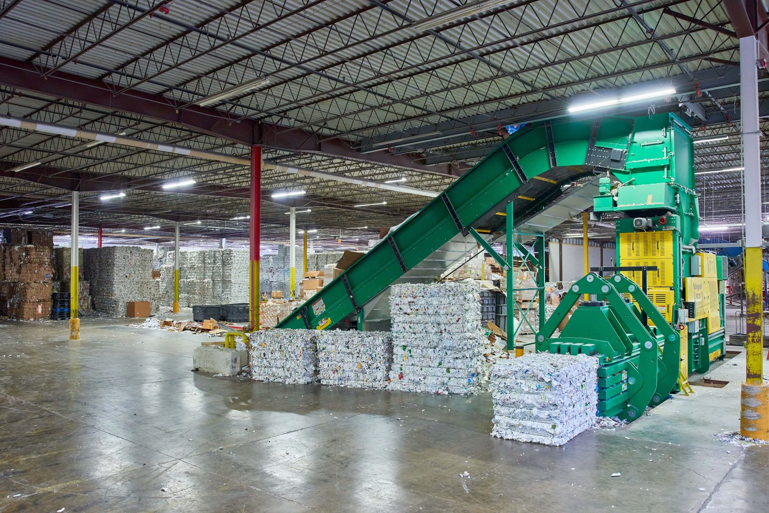 a warehouse with a conveyor belt carrying stacks of cardboard